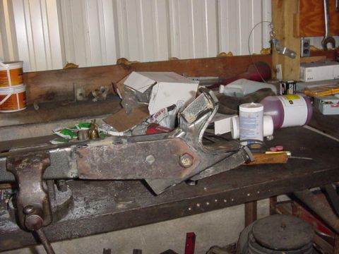 1992 Ford Bronco - A fabricated steel bracket assembly with fresh weld beads and a large hinge pin bolt clamped in a bench vise on a shop workbench. Behind it…
