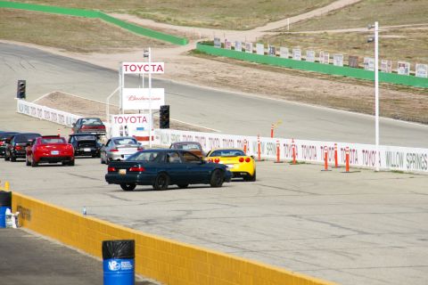 1995 Ford Taurus - A dark blue sedan leads a yellow Corvette on a race track with Toyota signage in the background.