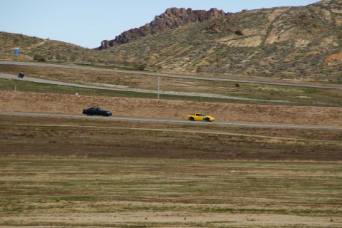 1995 Ford Taurus - Two cars driving on a race track with a mountainous backdrop.