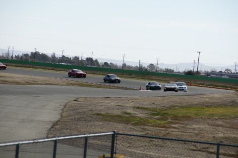 1995 Ford Taurus - Multiple vehicles compete on a paved race track under a clear sky.
