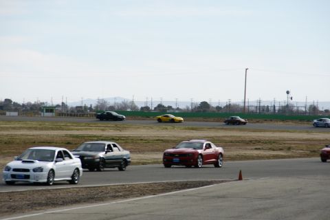 1995 Ford Taurus - Several cars are driving on a race track under a cloudy sky.