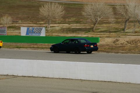 1995 Ford Taurus - A dark sedan is on a race track, with a yellow vehicle partially visible to the left.