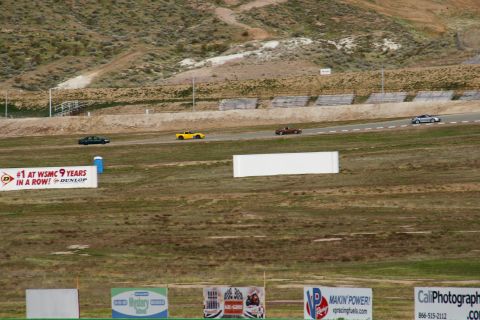 1995 Ford Taurus - Multiple cars race on a track with dry grass and hills in the background.