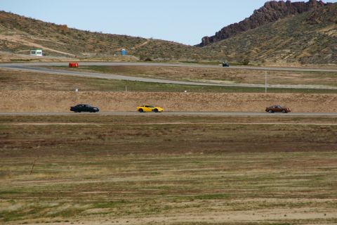 1995 Ford Taurus - Three cars are seen driving on a racetrack with a mountainous backdrop.