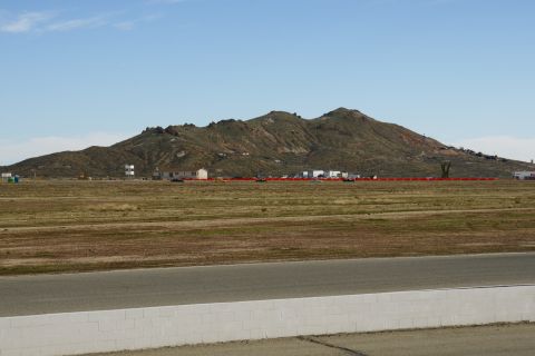 1995 Ford Taurus - A wide landscape shot shows a dry, grassy field with scattered buildings and a large mountain range under a clear blue sky.