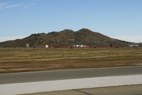 1995 Ford Taurus - Vehicles are scattered across a wide, open field with a mountain range under a clear blue sky.
