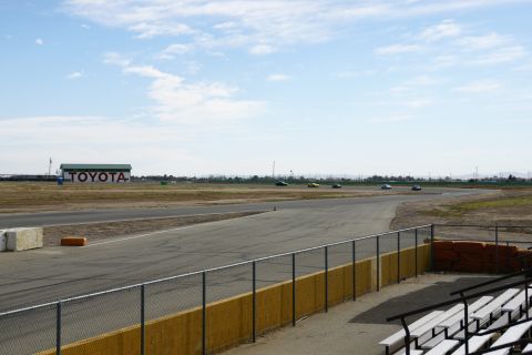 1995 Ford Taurus - Cars race on a track with a TOYOTA building in the background under a partly cloudy sky.
