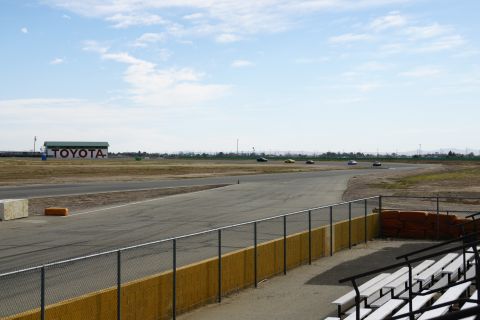 1995 Ford Taurus - A race track scene with multiple cars driving under a cloudy sky, a Toyota building visible in the distance.
