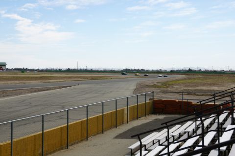 1995 Ford Taurus - Cars race on a track under a partly cloudy sky, with empty bleachers in the foreground.