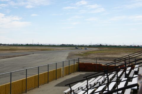 1995 Ford Taurus - Several cars are seen on a race track under a partly cloudy sky, with empty bleachers visible.