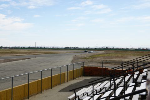 1995 Ford Taurus - Cars race on a track with grandstands in the foreground under a partly cloudy sky.