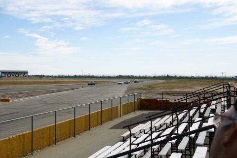 1995 Ford Taurus - Several cars are on a race track under a partly cloudy sky, with a Toyota building visible in the distance.