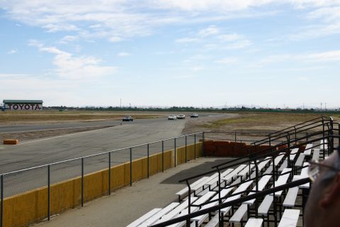 1995 Ford Taurus - Several cars race on a track under a partly cloudy sky, with a large Toyota building visible in the distance.