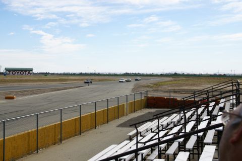 1995 Ford Taurus - Cars race on a track with Toyota branding visible on a distant building and bleachers in the foreground.