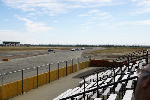 1995 Ford Taurus - Several cars are on a race track under a partly cloudy sky, with grandstands visible.
