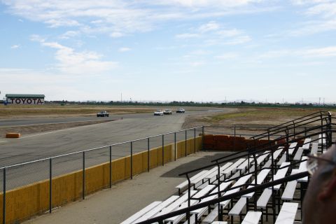 1995 Ford Taurus - Multiple vehicles compete on a race track under a partly cloudy sky, with a Toyota building visible in the distance.