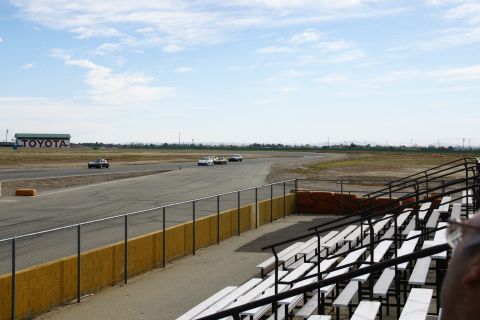 1995 Ford Taurus - Cars race on a track with bleachers and a TOYOTA building visible under a cloudy sky.