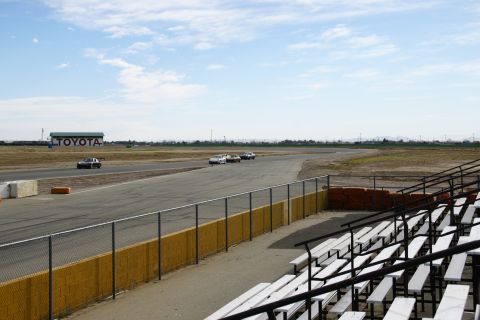 1995 Ford Taurus - Cars race on a track with a Toyota building visible in the distance under a partly cloudy sky.