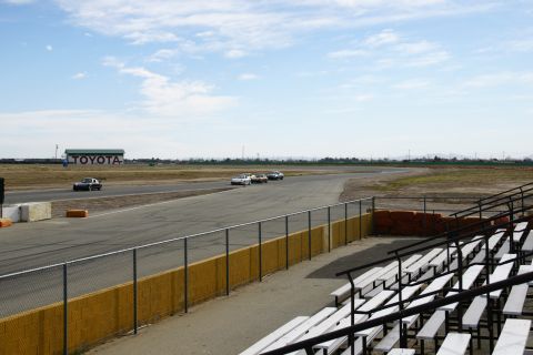 1995 Ford Taurus - Several cars are competing on a race track under a partly cloudy sky, with spectator seating visible.
