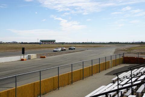 1995 Ford Taurus - Cars drive on a race track under a partly cloudy sky, with a Toyota building visible in the distance.