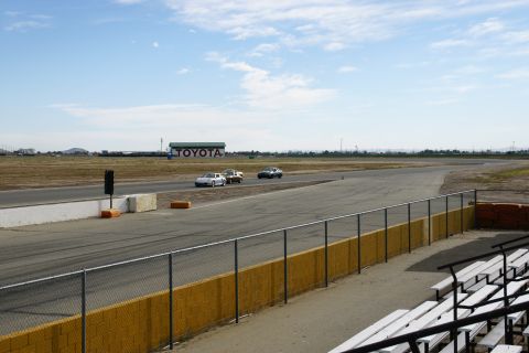 1995 Ford Taurus - Cars compete on a sunny day at a racetrack, with a large TOYOTA building visible in the distance.