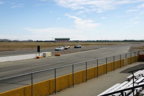 1995 Ford Taurus - Cars race on a track with a Toyota building visible in the distance under a partly cloudy sky.
