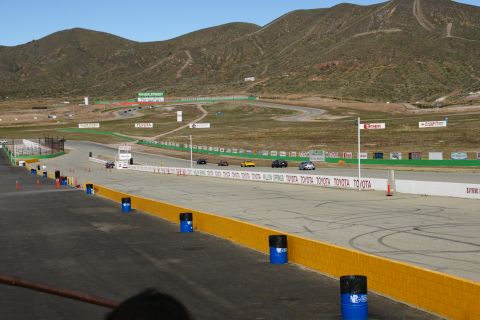 1995 Ford Taurus - A race track scene with multiple vehicles in motion under a clear sky, with mountainous terrain and sponsor signage visible.