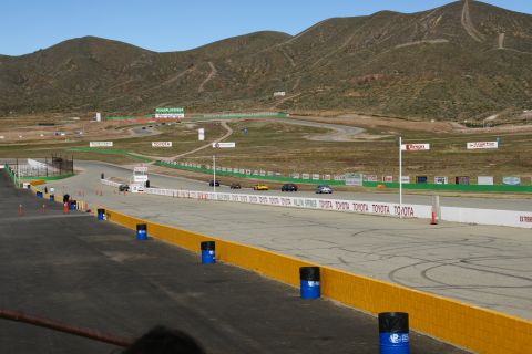 1995 Ford Taurus - A view of a race track with several cars driving on it, set against a backdrop of hills under a clear sky.