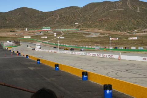 1995 Ford Taurus - A view of a race track with multiple cars driving, set against a backdrop of rolling hills and mountains.