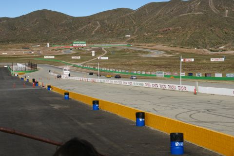 1995 Ford Taurus - A race track with several cars on it, set against a backdrop of dry, rolling hills under a clear sky.
