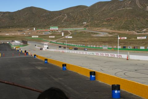 1995 Ford Taurus - A race track scene with multiple vehicles visible on the course, set against a backdrop of rolling hills and mountains.