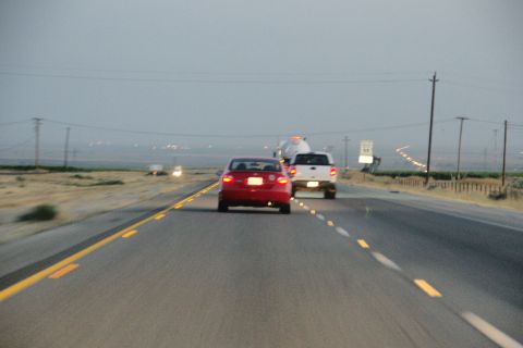 1995 Ford Taurus - Two vehicles travel down a highway as the sky darkens, with a speed limit sign visible in the distance.