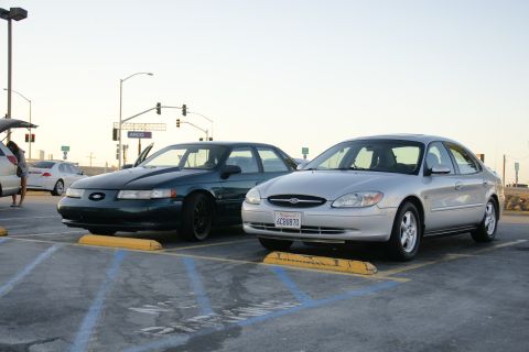 1995 Ford Taurus - Two Ford Taurus sedans are parked in a lot, one silver and one dark green.