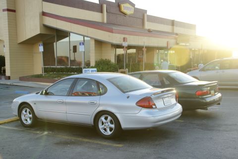 1995 Ford Taurus - A silver 1995 Ford Taurus sedan is parked in a lot, with a Denny's restaurant in the background.