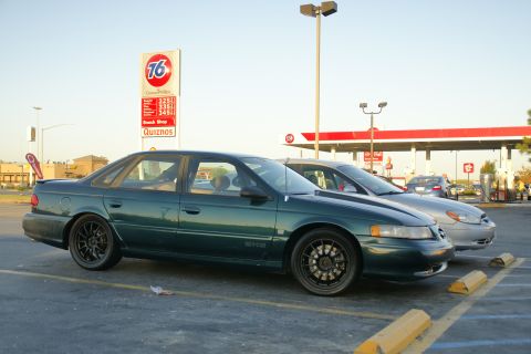 1995 Ford Taurus - A dark green 1995 Ford Taurus sedan is parked next to another car at a gas station.