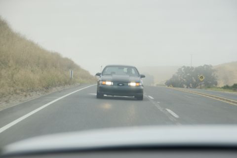 1995 Ford Taurus - A dark 1995 Ford Taurus drives down a highway on a foggy day.
