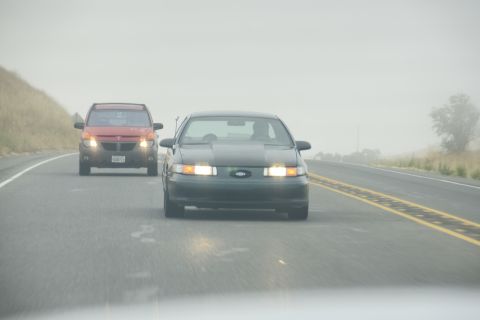 1995 Ford Taurus - A dark sedan drives on a foggy highway, with another vehicle visible ahead.