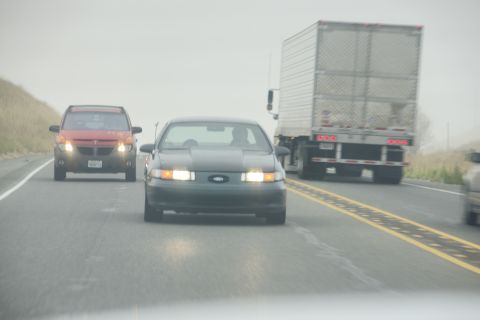 1995 Ford Taurus - A dark 1995 Ford Taurus sedan is seen on the highway, with a red SUV and a semi-truck also on the road.