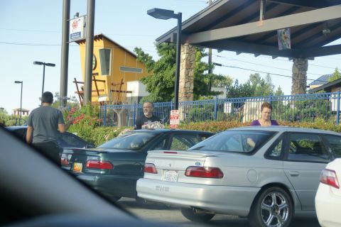 1995 Ford Taurus - Two sedans are parked outside a building with people visible inside and around them.
