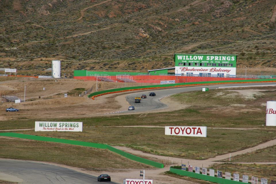 Cars racing on a track at Willow Springs, with grandstands and signs