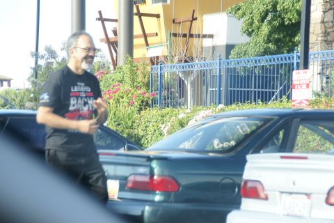 1995 Ford Taurus - Man walks past parked cars in front of a building with landscaping.