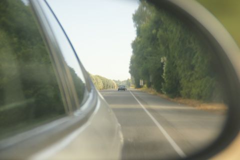 1995 Ford Taurus - View from a car's side mirror shows another vehicle on a tree-lined road.
