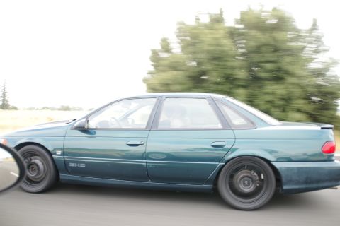 1995 Ford Taurus - A teal sedan is captured in motion on a road, with trees blurred in the background due to its speed.