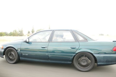 1995 Ford Taurus - A green 1995 Ford Taurus sedan is captured in a side profile shot, showing its distinctive body style and black wheels.