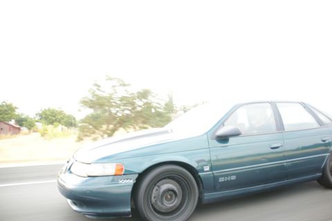 1995 Ford Taurus - A teal 1995 Ford Taurus SHO sedan is captured in motion on a highway, its side profile.