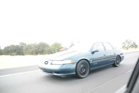 1995 Ford Taurus - A teal 1995 Ford Taurus sedan is captured in a 3q-front view while driving on a highway.