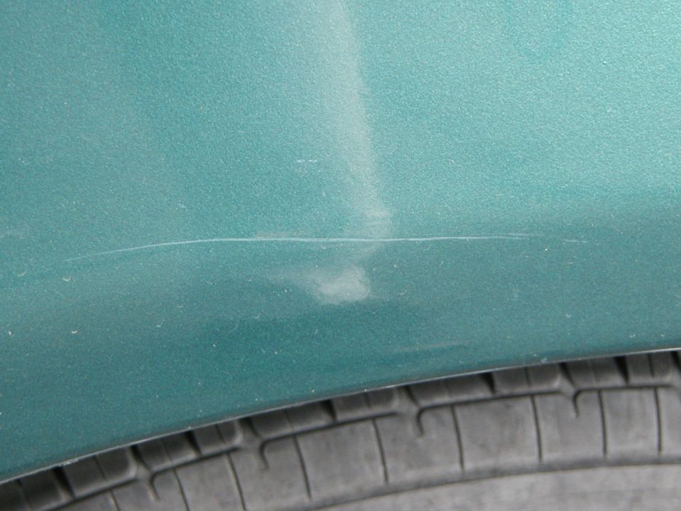 Close-up of scratches and scuff marks on teal green car body panel above a tire