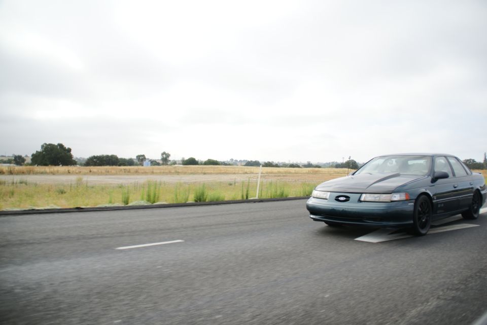 Dark green sedan driving on a road, front 3/4 view