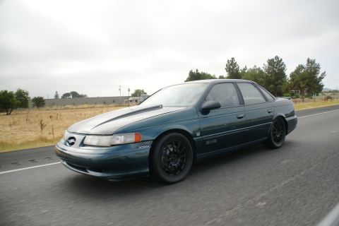 1995 Ford Taurus - A dark green 1995 Ford Taurus SHO with aftermarket wheels and a hood scoop is seen driving on a highway.