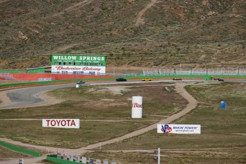 1995 Ford Taurus - Multiple vehicles race on a track with grandstands and sponsor signage under a hilly landscape.